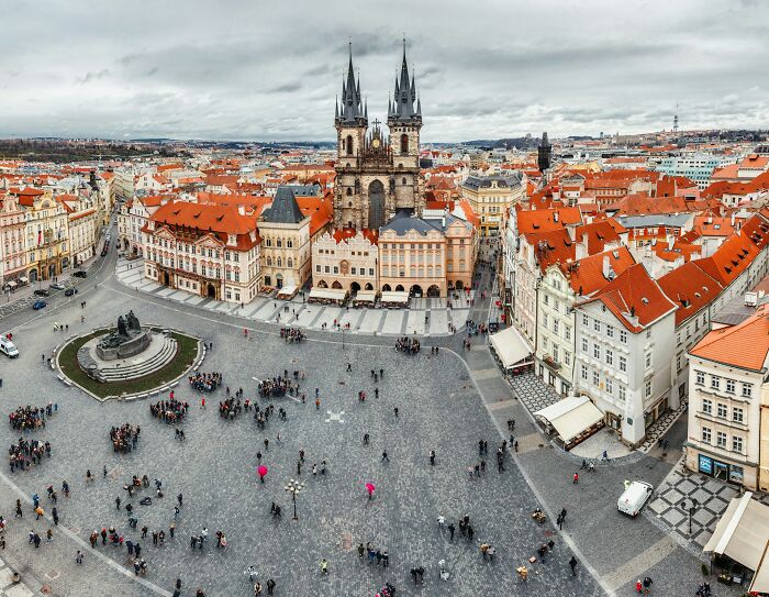 Aerial view of a European town square with tourists, historic buildings, and notable church towers in a popular travel destination.