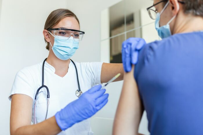 Close-up of a healthcare worker wearing gloves giving a vaccine injection to a person's upper arm.