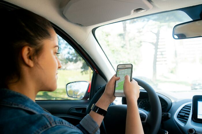 Millennial using smartphone for navigation inside car, illustrating industries impacted by millennial behavior shifts.