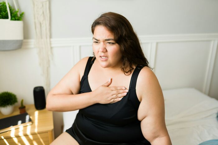 Woman in black tank top showing discomfort while holding chest, illustrating frustrating experiences with dismissive doctors.