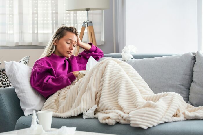 Woman wrapped in blanket sitting on couch looking tired surrounded by tissues depicting postpartum OCD struggles.