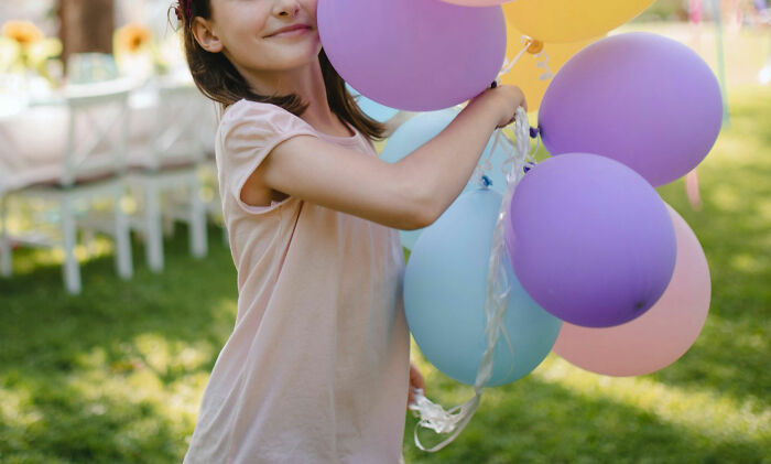Young girl holding colorful balloons outdoors, illustrating childhood experiences linked to worst parents seen.