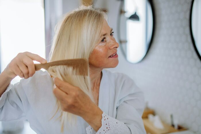 Woman over 42 with blonde hair combing in front of mirror, representing women over 42 no longer tolerating old limits