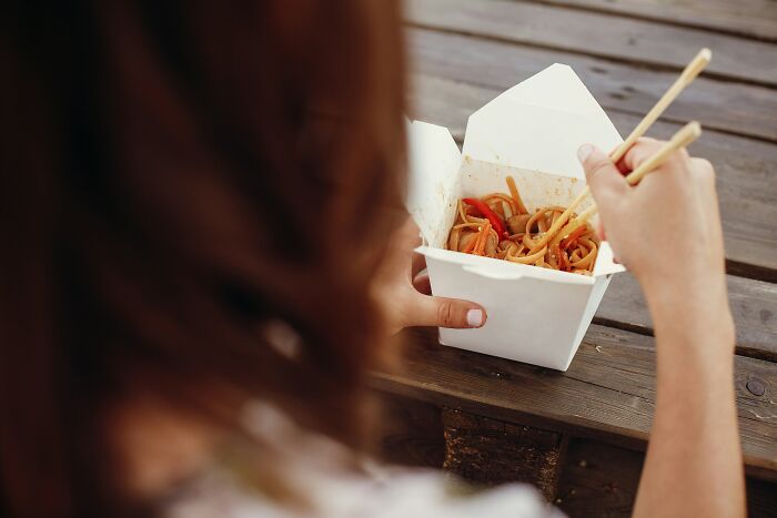 Person using chopsticks to eat Asian takeout noodles, illustrating foreigners' experiences of being big in Japan.