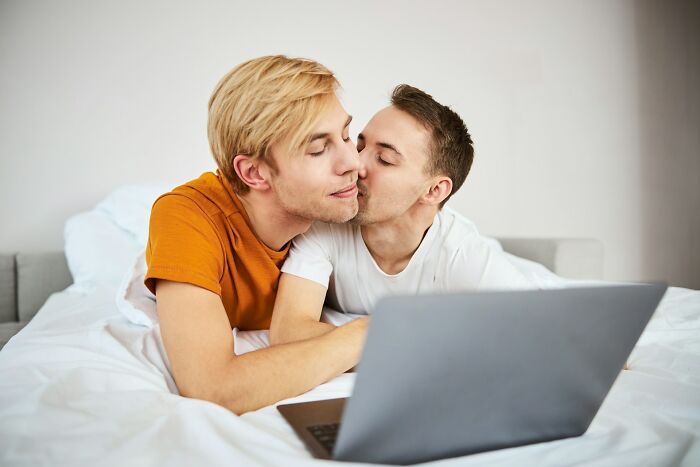 Two men sharing a tender moment on a bed with a laptop, illustrating secrets people keep from their lovers.