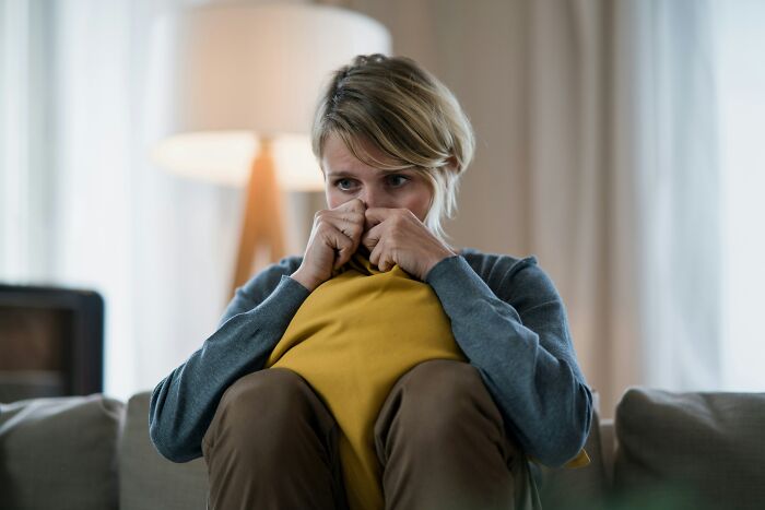 Woman sitting on couch holding a pillow, showing signs of anxiety related to postpartum OCD in a softly lit room.