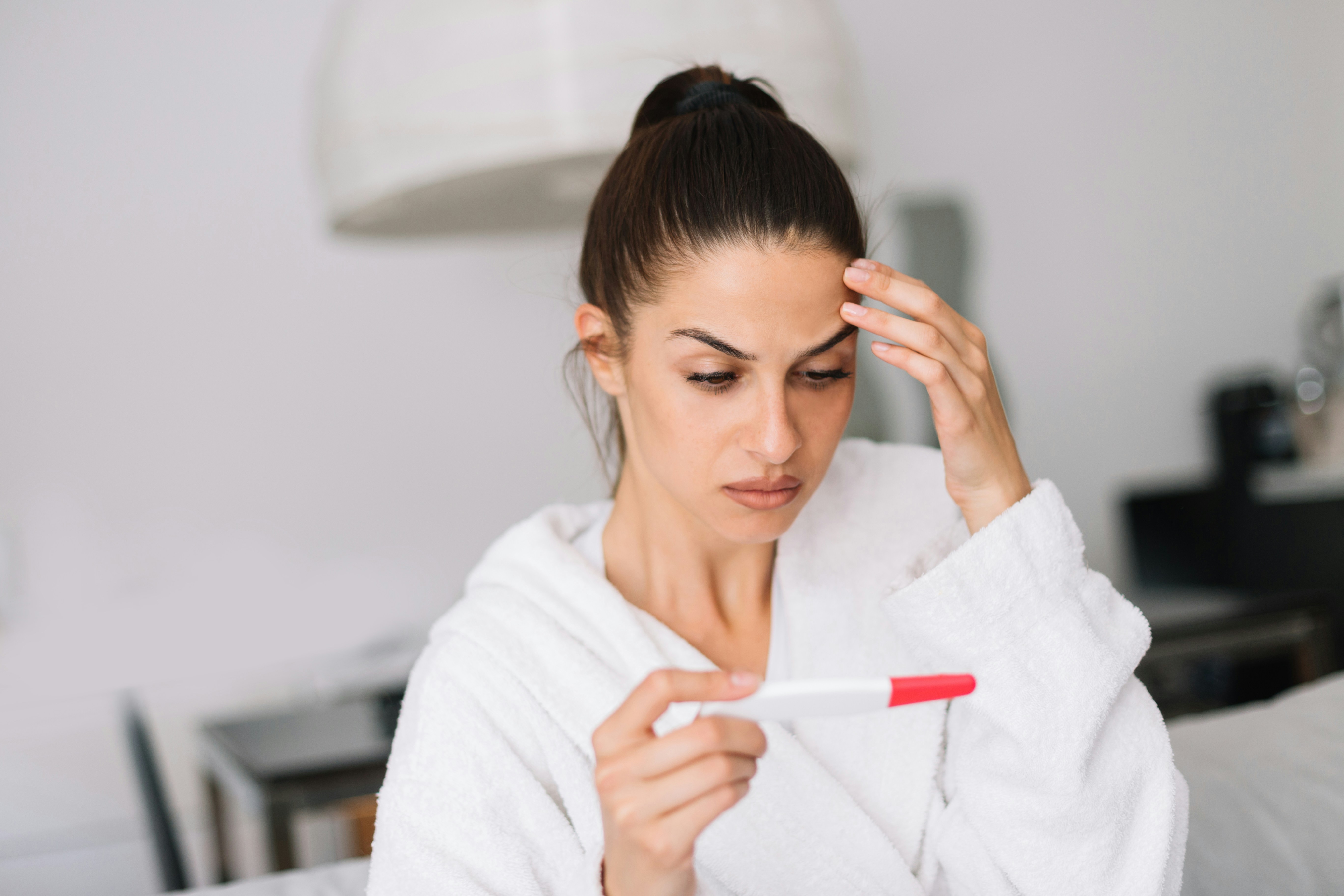 Woman in a white robe looks concerned holding a pregnancy test, standing her ground after roommate demands nursery space Woman in a white robe looks concerned holding a pregnancy test, standing her ground after roommate demands nursery space