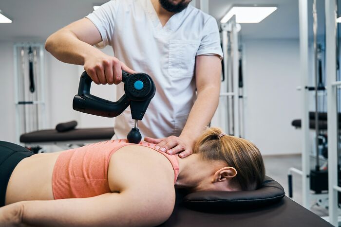 Woman receiving shoulder treatment with a massage gun from a healthcare professional in a clinical setting related to dismissive doctors.