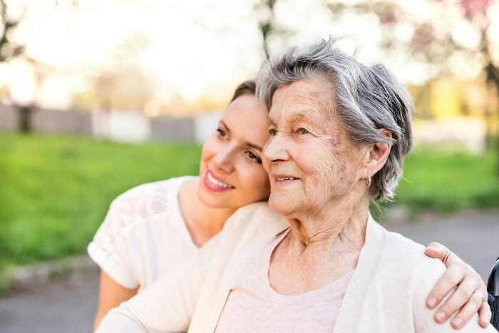 Younger woman hugging elderly woman outdoors, showing support and care in an emotional moment of getting back at cheating exes.