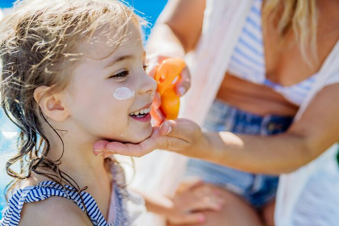 Young girl smiling while getting sunscreen applied, promoting healthy habits and avoiding tobacco use for better health.