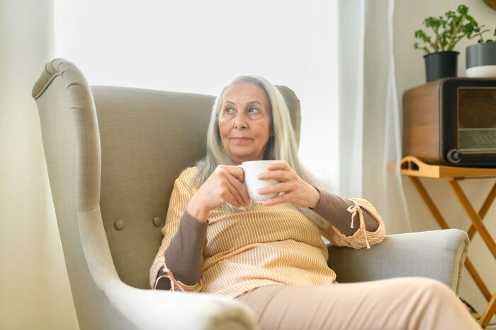 Mature woman over 42 sitting in an armchair, holding a cup, reflecting on what she’s no longer willing to tolerate.