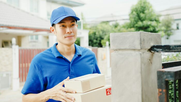 Delivery worker in a blue uniform holding packages outside a residential gate, illustrating moments police got dragged into nonsense.