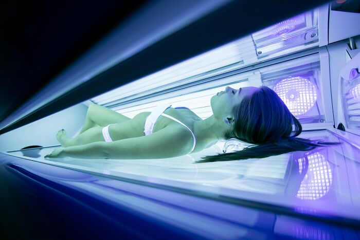 Woman lying in a tanning bed under ultraviolet lights, highlighting skin care and risks of tobacco use.