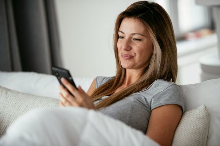 Woman reclining on a couch, looking at her phone with a satisfied expression, symbolizing getting back at cheating exes.