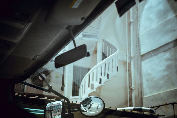 Interior view from inside a vehicle looking out at a white spiral staircase and building exterior, symbolizing one wrong deed.