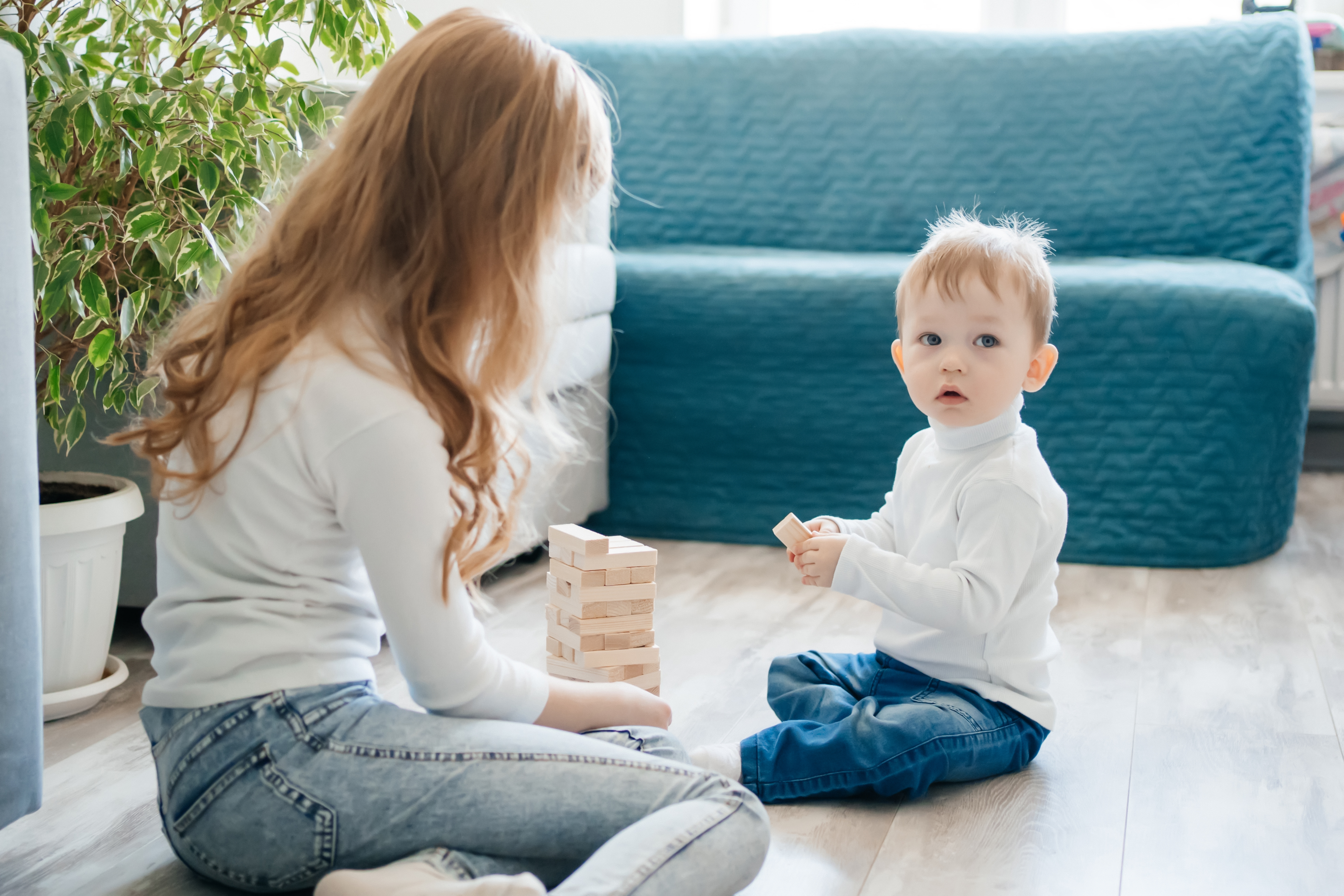 Young woman babysitting child at home playing with wooden blocks on floor during summer care time