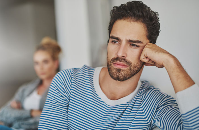Man looking thoughtful and concerned while woman in background shows signs of girlfriend behaviour change in relationship.