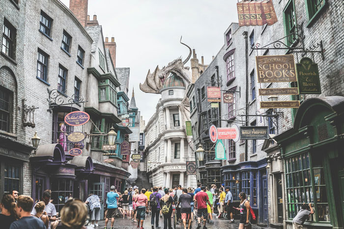 Crowded Harry Potter Wizarding World street with shops and a dragon perched above, linked to man accused of supporting transphobia.