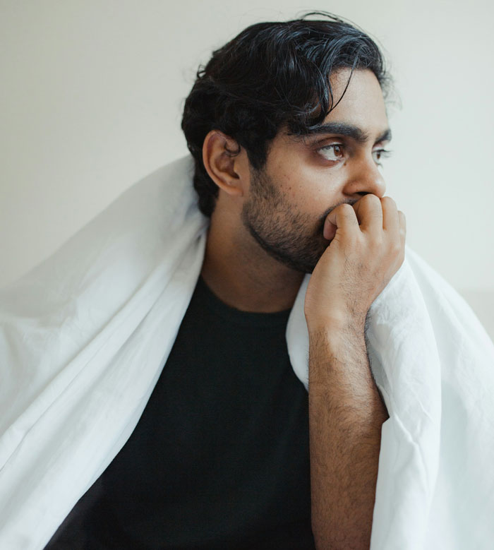 Man wrapped in a white blanket looking thoughtful, portraying a man accused of supporting transphobia in Harry Potter Wizarding World.