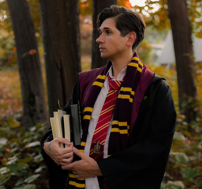 Man dressed as a Harry Potter character in wizarding world attire, holding books in a forest setting.