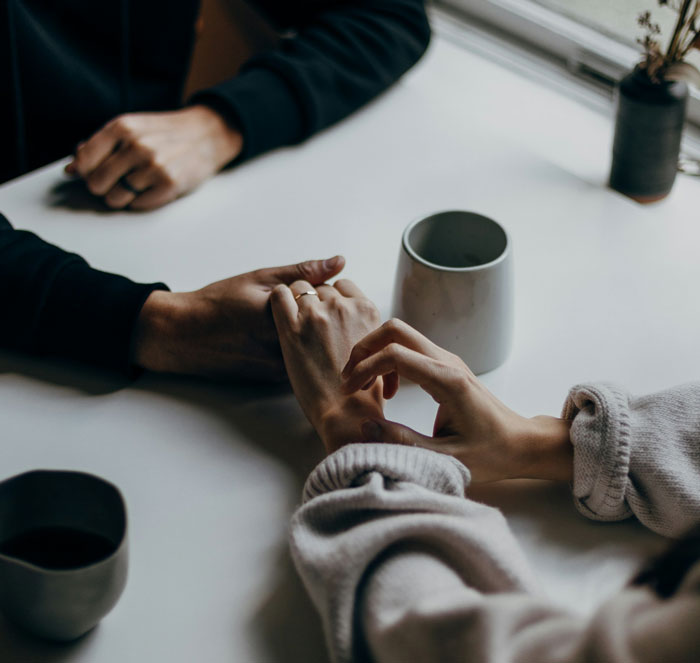Two people holding hands at a table with cups, illustrating support in the context of man accused of supporting transphobia.
