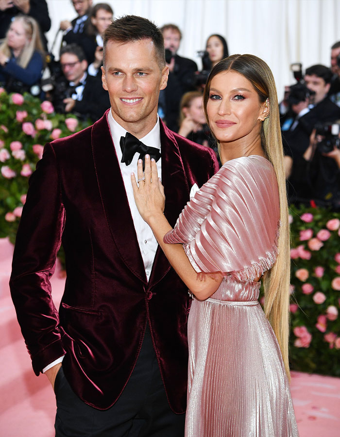 Tom Brady and Gisele Bundchen posing on the red carpet at a formal event with photographers in the background.