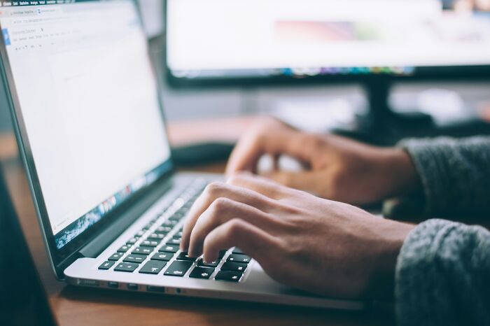 Hands typing on a laptop keyboard with a blurred desktop monitor in the background, illustrating shared knowledge topics.