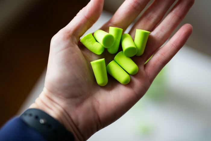 Hand holding multiple bright green earplugs illustrating a useful golden travel hack for noise reduction while traveling.