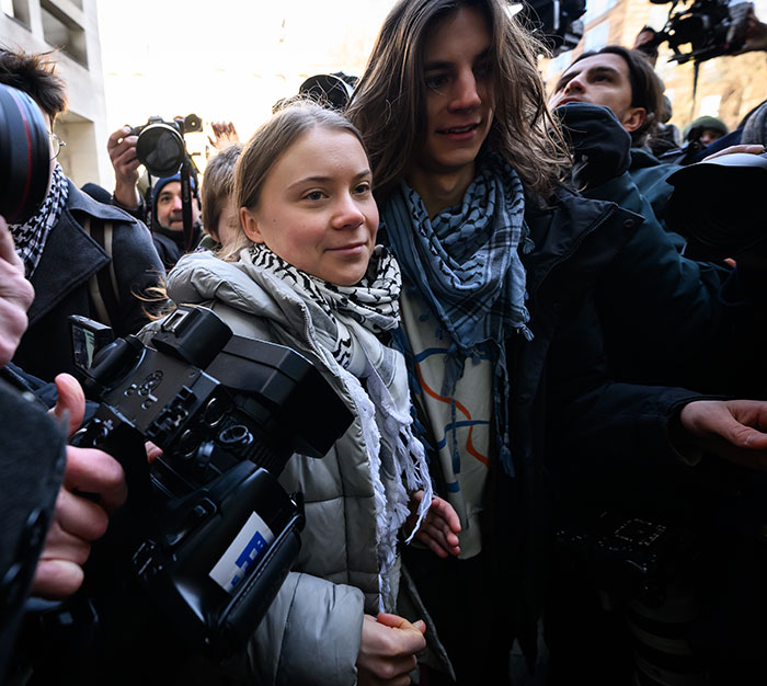 Greta Thunberg with Chris Kebbo surrounded by photographers and media in an outdoor crowd setting.