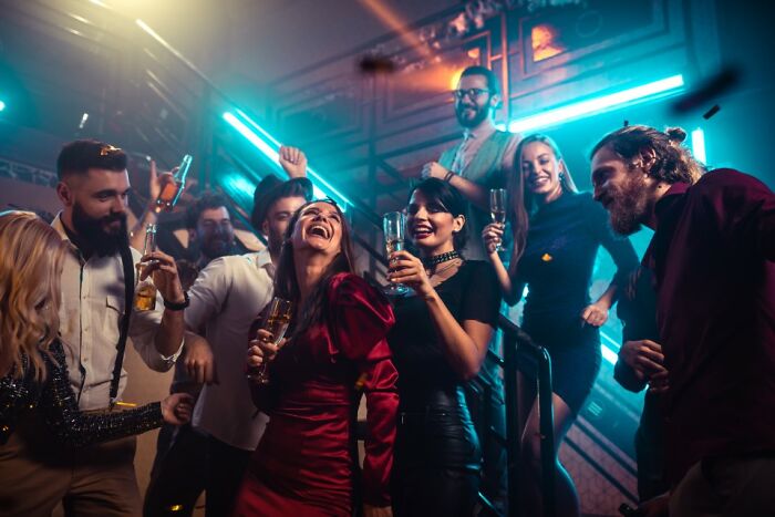 Group of stylish rich people flaunting their wealth at a vibrant party with drinks and neon lights in an upscale setting