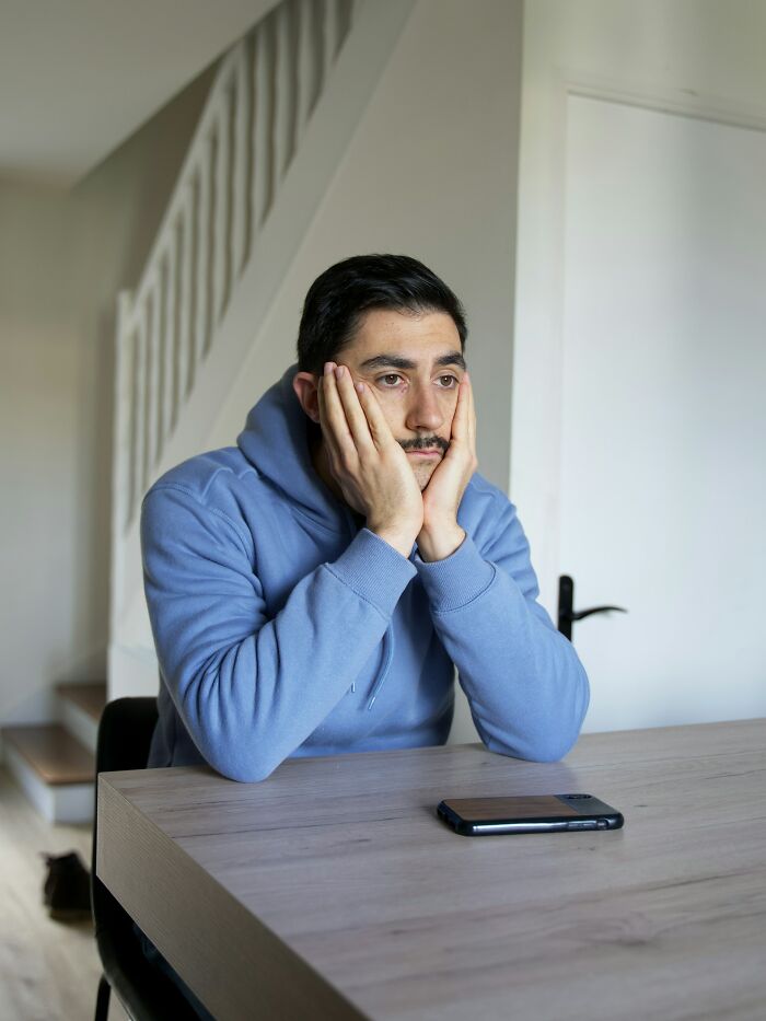 Man in blue hoodie sitting at table looking upset, illustrating moments people realized their close friend was actually a total jerk.