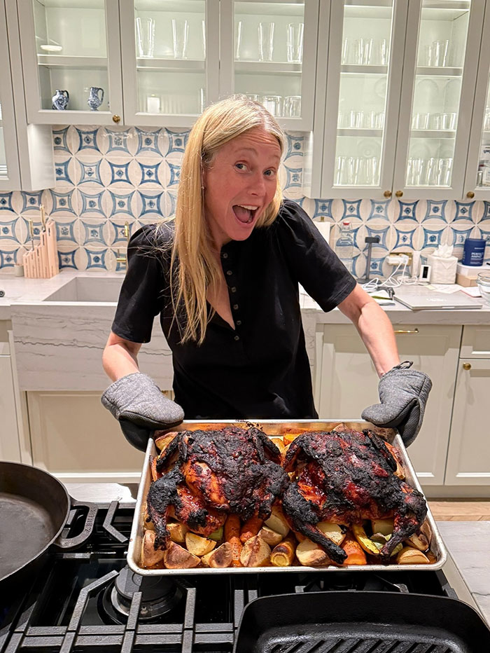 Woman holding a tray of roasted chickens in kitchen, related to Apple Martin roasting mom Gwyneth Paltrow cooking post backlash. Woman holding a tray of roasted chickens in kitchen, related to Apple Martin roasting mom Gwyneth Paltrow cooking post backlash.