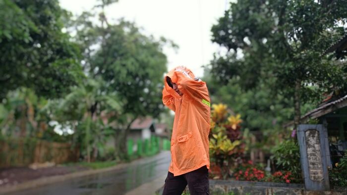 Person in orange raincoat covering their face in rainy outdoor setting, illustrating big no no to do in your country.