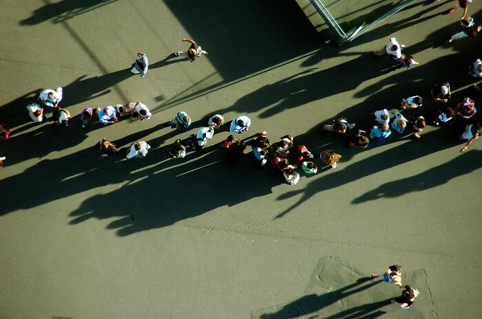 Aerial view of people standing and walking on pavement casting long shadows, illustrating cultural no no to do in your country.