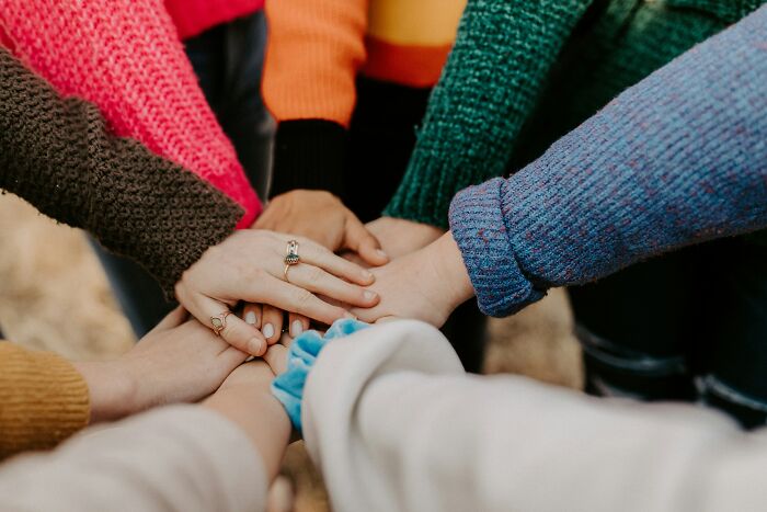 Group of people wearing colorful sweaters placing hands together symbolizing teamwork and famous paradoxes concept.