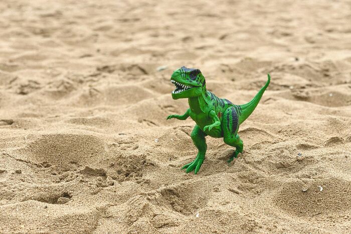 Green toy dinosaur standing on sandy ground representing dinosaur facts and prehistoric creatures.