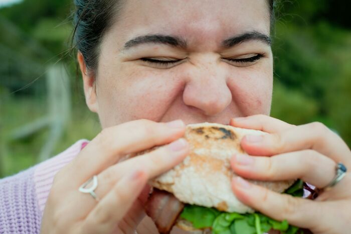 Person enjoying a large sandwich outdoors, capturing a candid moment related to spicy and heartfelt secrets.