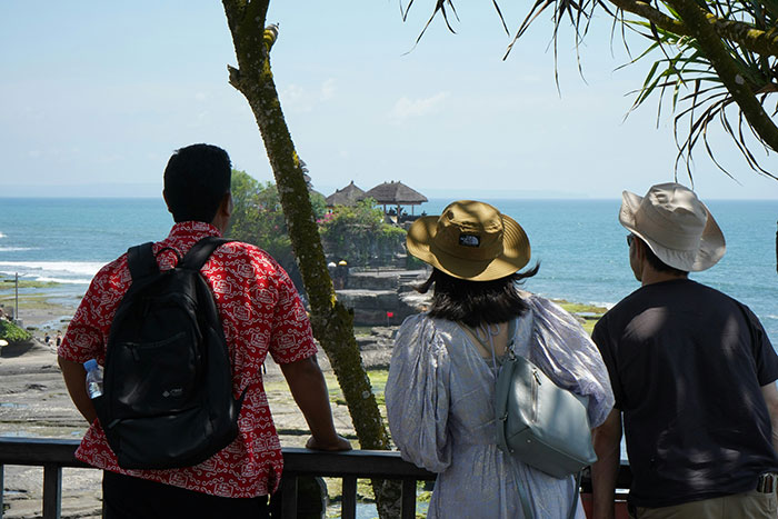 Three tourists overlooking a tropical coastal temple, highlighting realities of living in tropical places many dream of.