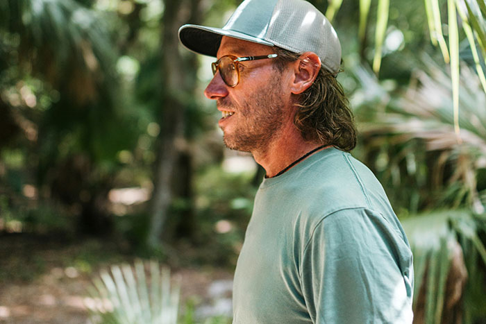 Man wearing cap and glasses outdoors in tropical places, reflecting on realities of living in tropical areas.