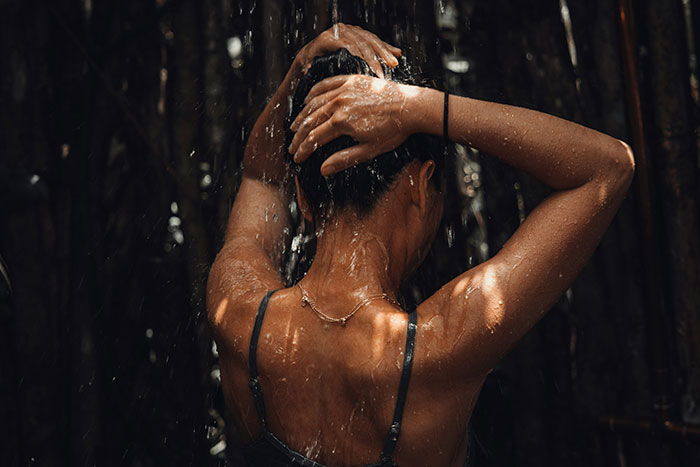 Woman rinsing hair under outdoor shower, highlighting realities of living in tropical places with intense sunlight and humidity.