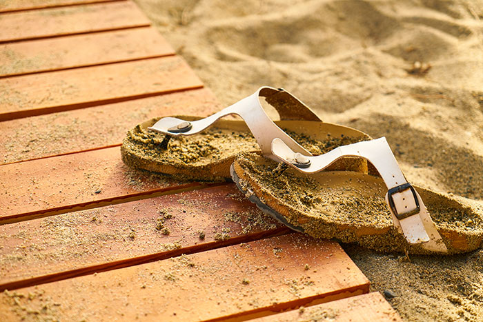 White sandals covered in sand on a wooden boardwalk, illustrating realities of living in tropical places many dream of.