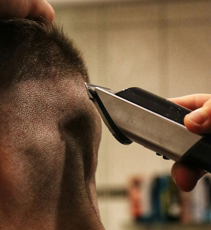 Close-up of hair clippers shaving the side of a man's head, illustrating the concept of targeting fat areas.
