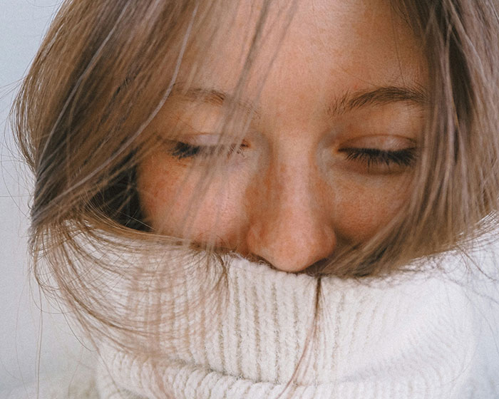 Young woman with closed eyes wearing a cozy white sweater, representing wellness and targeting fat awareness.