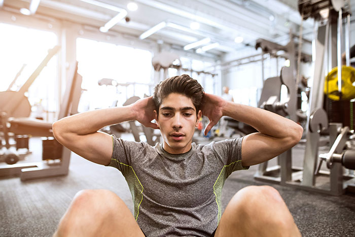 Young man targeting fat by doing sit-ups in a gym setting focused on health and wellness workout routine.