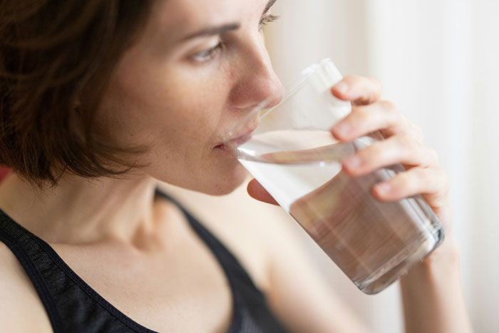 Woman in a black tank top drinking a glass of water focusing on health and wellness myths about targeting fat.