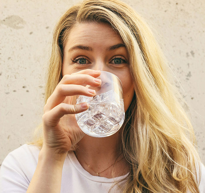 Young woman with long blonde hair drinking water, illustrating debunked health and wellness myths about targeting fat.