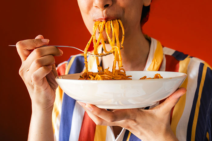 Person eating pasta from a white bowl, illustrating common fat targeting and health and wellness myths.