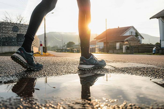 Person walking on pavement near a puddle at sunrise, illustrating fitness and health targeting fat effectively.
