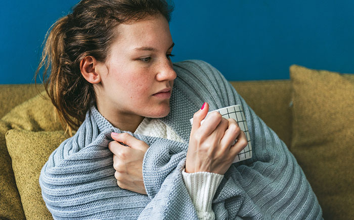 Young woman wrapped in a gray blanket holding a mug, illustrating comfort while discussing targeting fat and wellness myths.
