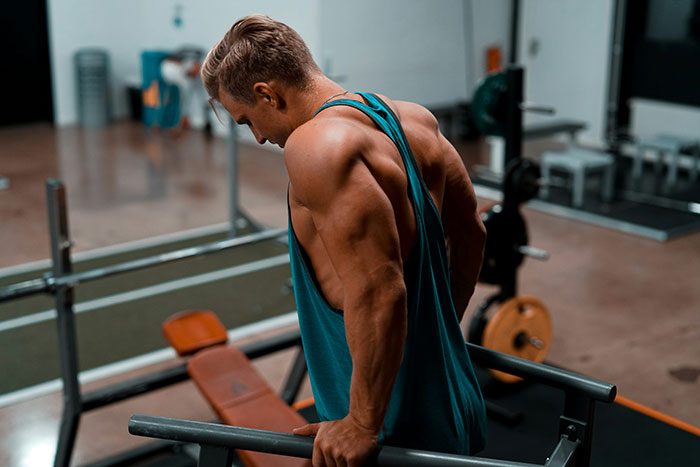 Man with muscular back and arms exercising on parallel bars in gym, illustrating fat targeting and fitness concepts.